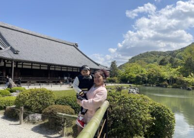 Smiling Mari is holding tired-looking Lucas in her arms against the backdrop of the temple and the lake.